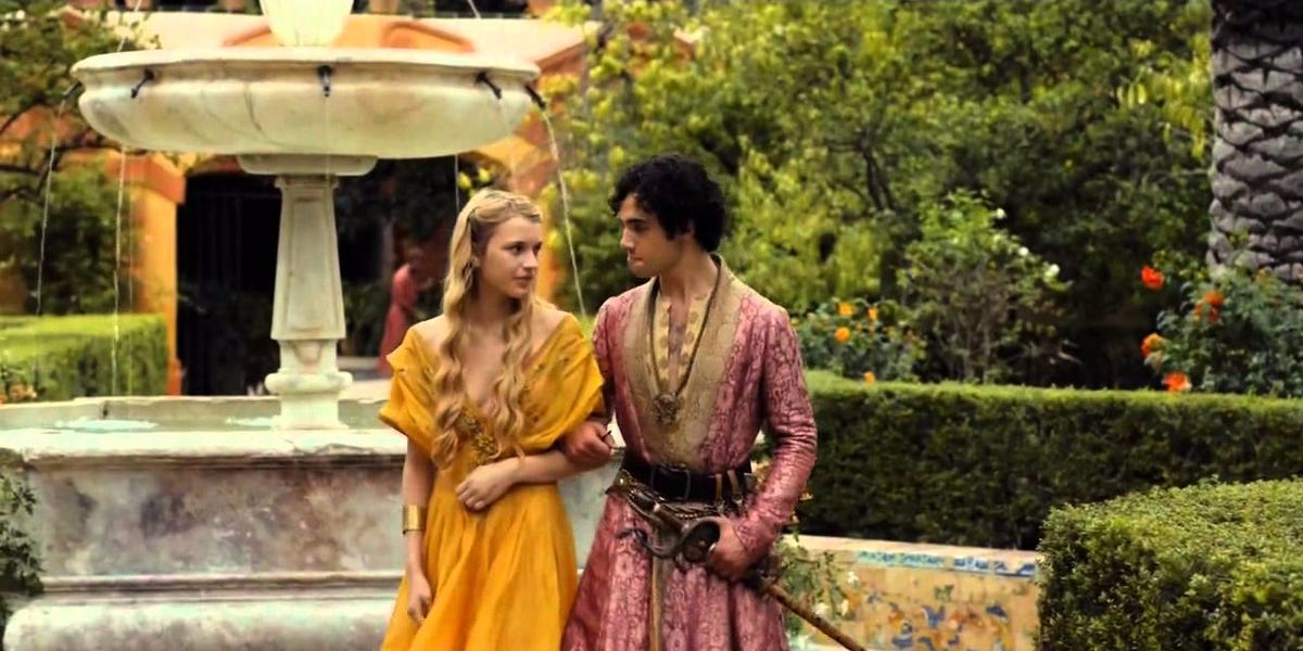 Myrcella Baratheon walking arm locked on Trystane Martell with the palace garden and fountain in the backdrop