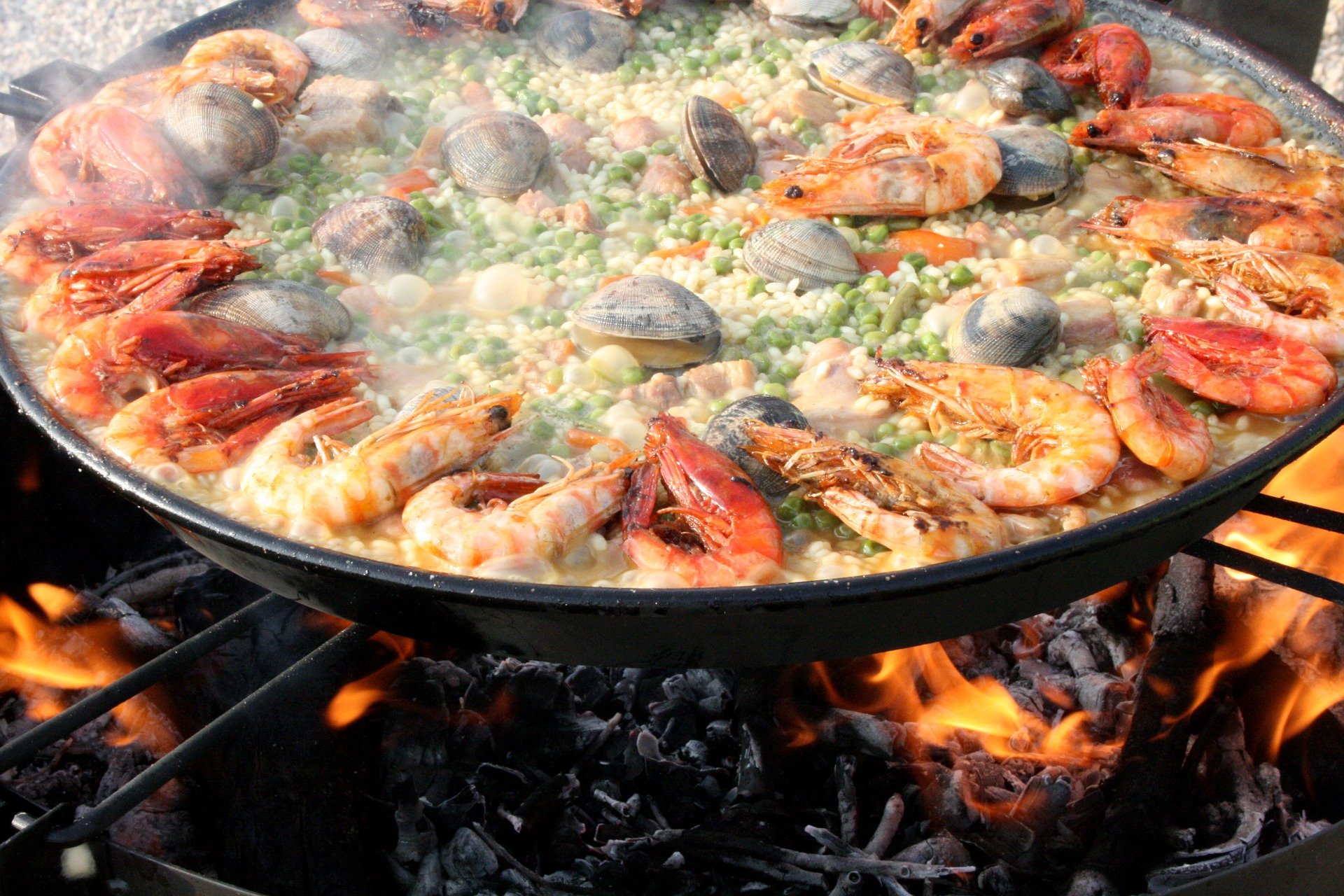 A Paella being prepared in a big frying pan on a barbecue grill