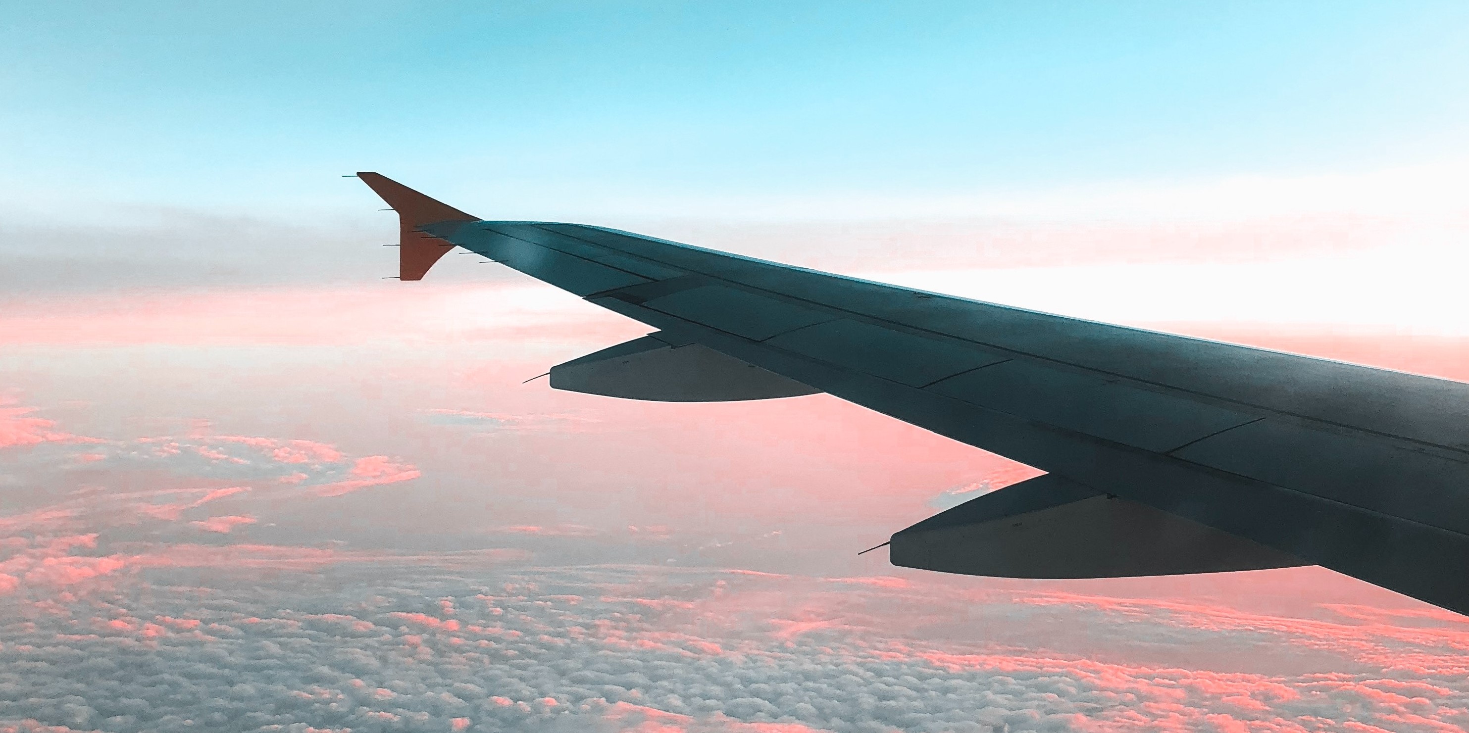 L'ala di un aereo sopra alcune nuvole con sfumature blu e rosa
